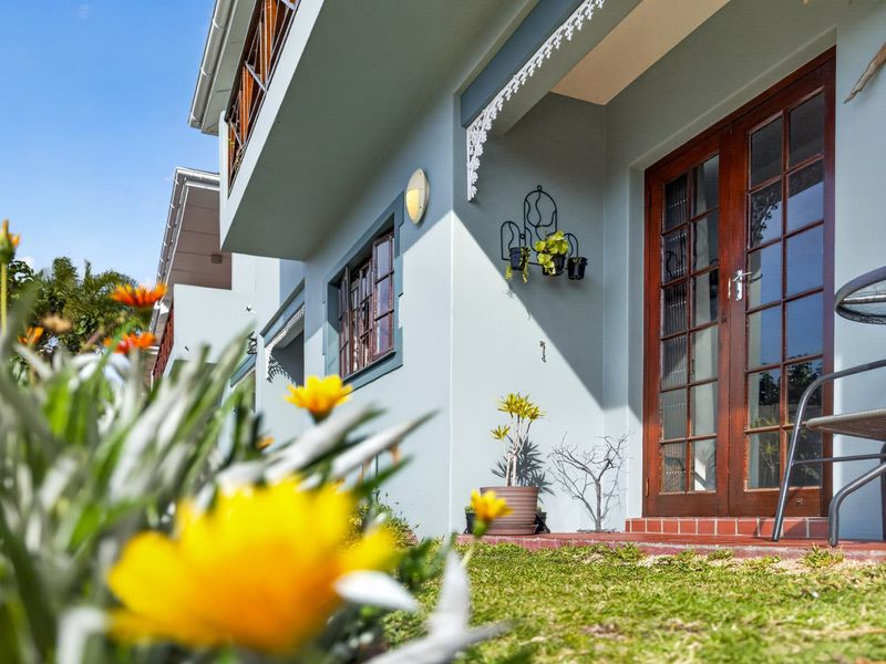 A well-maintained rear exterior view of the apartment featuring timber-framed glass doors, decorative eaves, and a neat garden area.