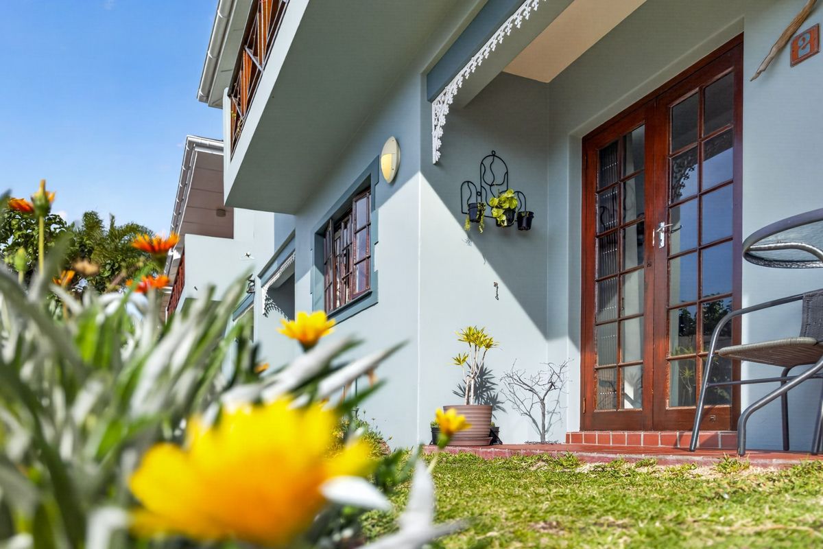 A well-maintained rear exterior view of the apartment featuring timber-framed glass doors, decorative eaves, and a neat garden area.