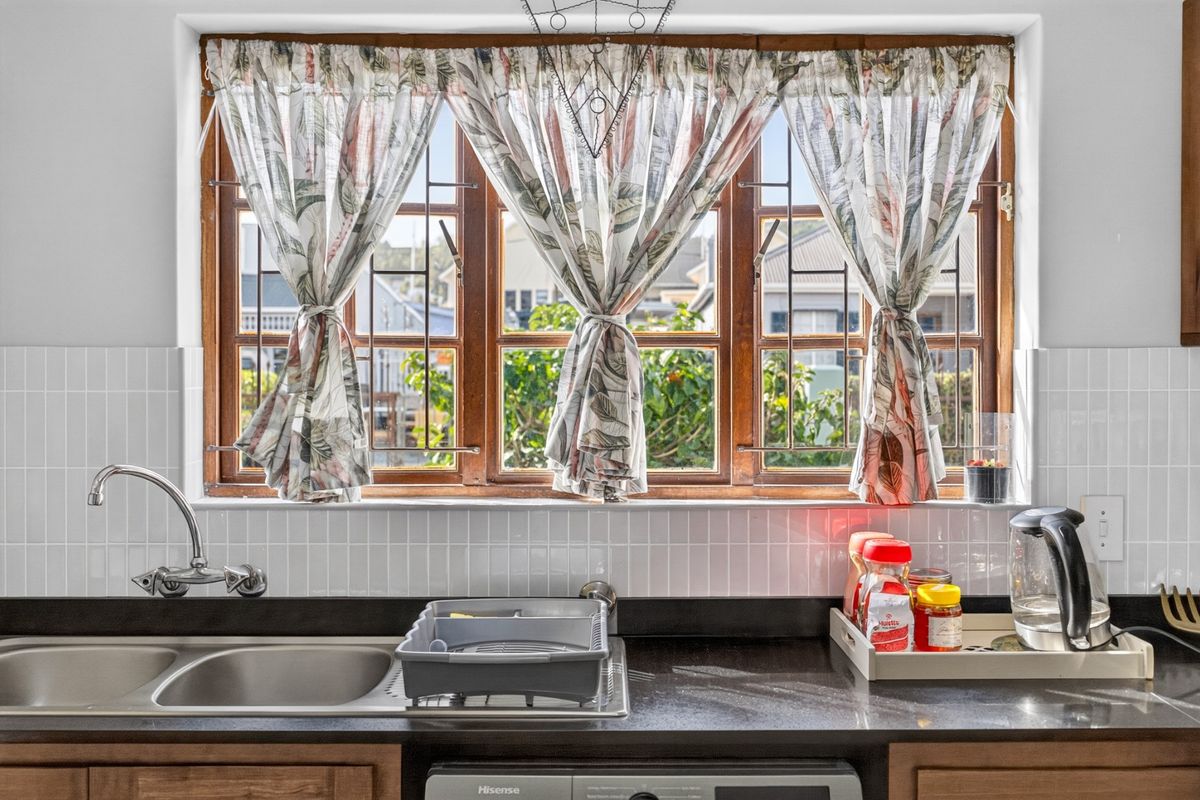 A functional kitchen area featuring a double bowl stainless steel sink, dark stone countertops, and a classic white subway tile backsplash under a wooden window.