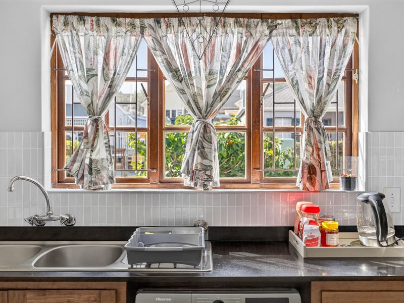 A functional kitchen area featuring a double bowl stainless steel sink, dark stone countertops, and a classic white subway tile backsplash under a wooden window.