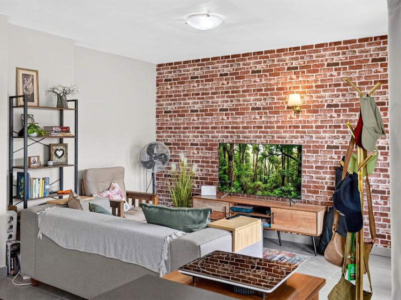 A cozy living room featuring a prominent exposed brick accent wall, neutral tiled flooring, and integrated wall lighting.