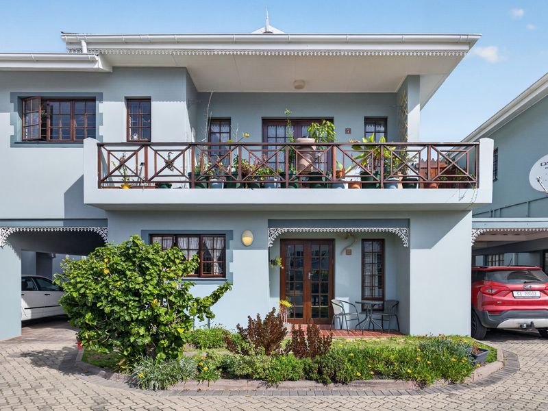 Front elevation of a two-story apartment featuring a balcony with timber balustrades, paved driveway, and integrated carport parking.