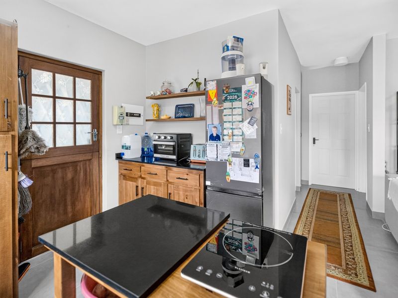 A functional kitchen area featuring wooden cabinetry, black granite countertops, an induction cooktop, and a classic wooden door with glass panes.