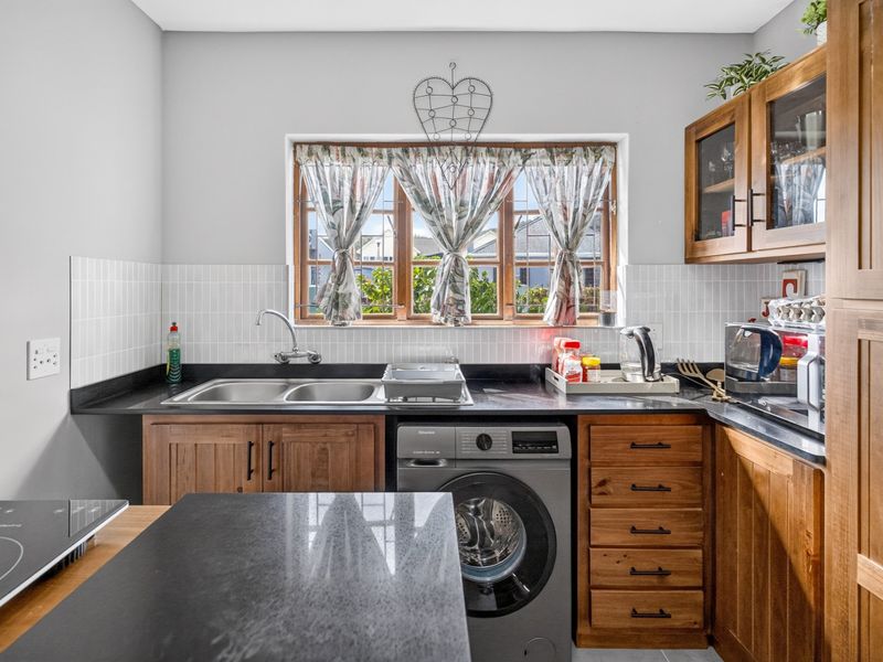 A functional kitchen featuring wooden cabinetry, a double sink with mixer tap, tiled backsplash, and a built-in washing machine under the countertop.