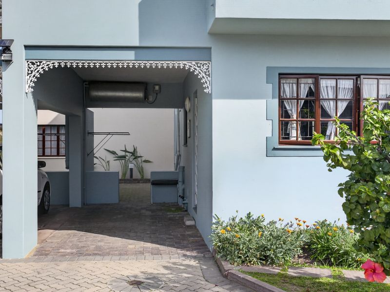 Front elevation of the apartment featuring a paved driveway, covered carport area with decorative fretwork, and timber-framed windows.