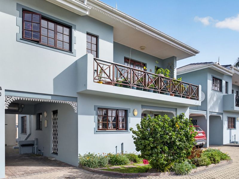 Front elevation of a multi-story apartment building featuring a balcony with timber balustrades, paved driveway, and decorative architectural detailing.