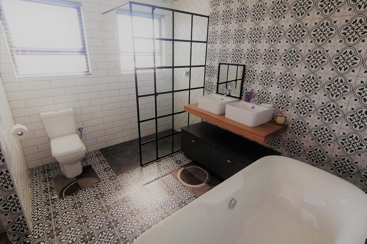 Modern bathroom featuring a freestanding bathtub, walk-in shower with black frame, double vanity with vessel sinks, and stylish patterned tile accents.