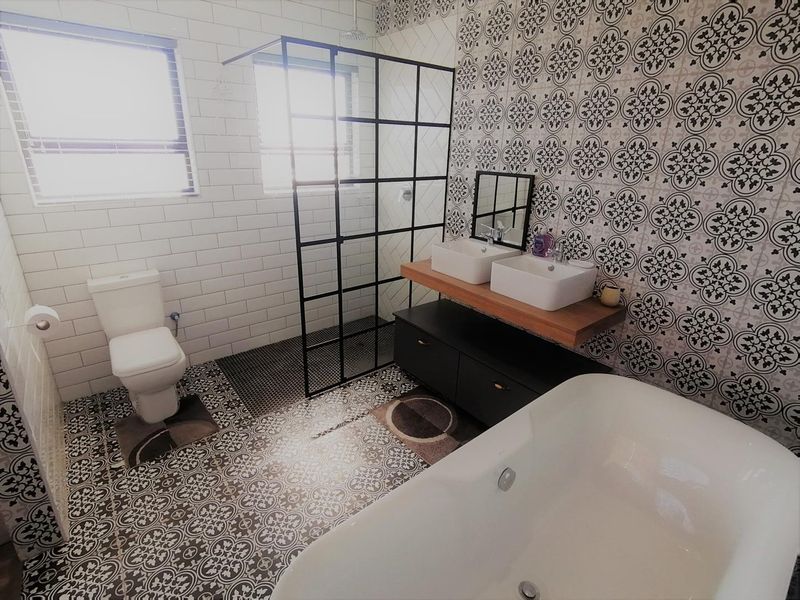 Modern bathroom featuring a freestanding bathtub, walk-in shower with black frame, double vanity with vessel sinks, and stylish patterned tile accents.