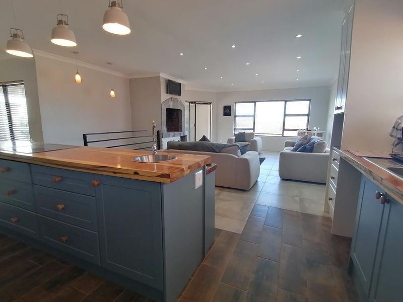 Spacious open-plan living area featuring a modern kitchen with a timber-topped island, stone fireplace, and neutral tiled flooring throughout.
