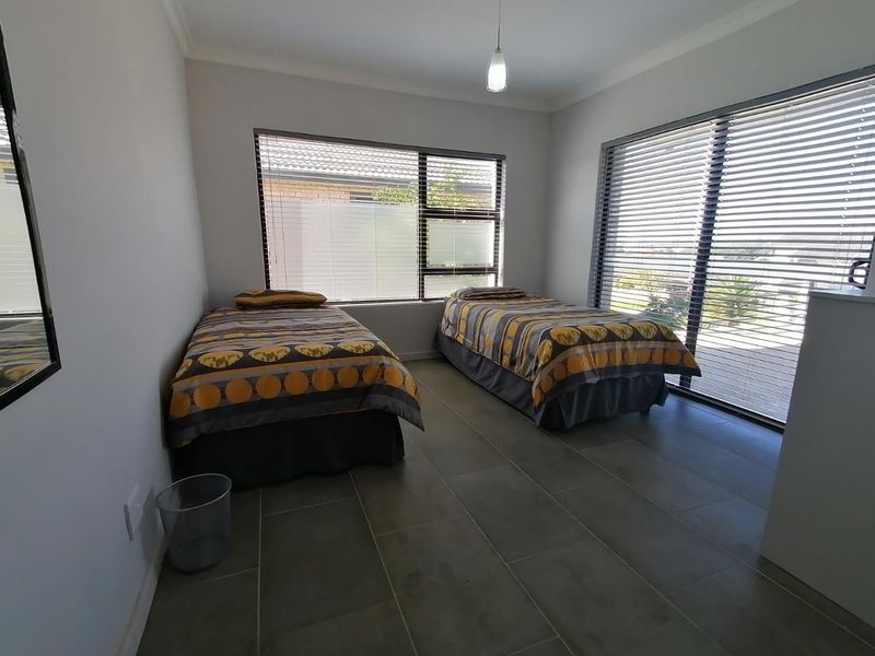 A bright bedroom featuring large windows with venetian blinds, tiled flooring, and a sliding door providing access to the exterior.