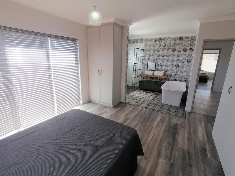 Modern bedroom featuring an open-plan en-suite bathroom with a freestanding bathtub, double vanity, and walk-in shower, complemented by stylish patterned tiling and laminate flooring.