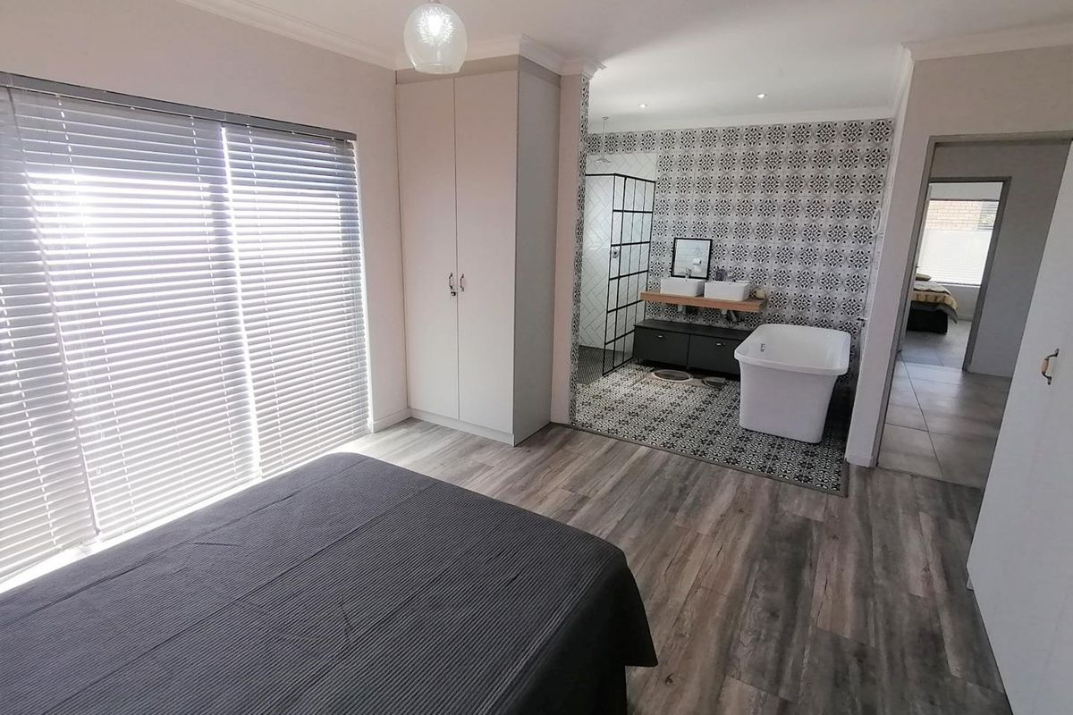 Modern bedroom featuring an open-plan en-suite bathroom with a freestanding bathtub, double vanity, and walk-in shower, complemented by stylish patterned tiling and laminate flooring.