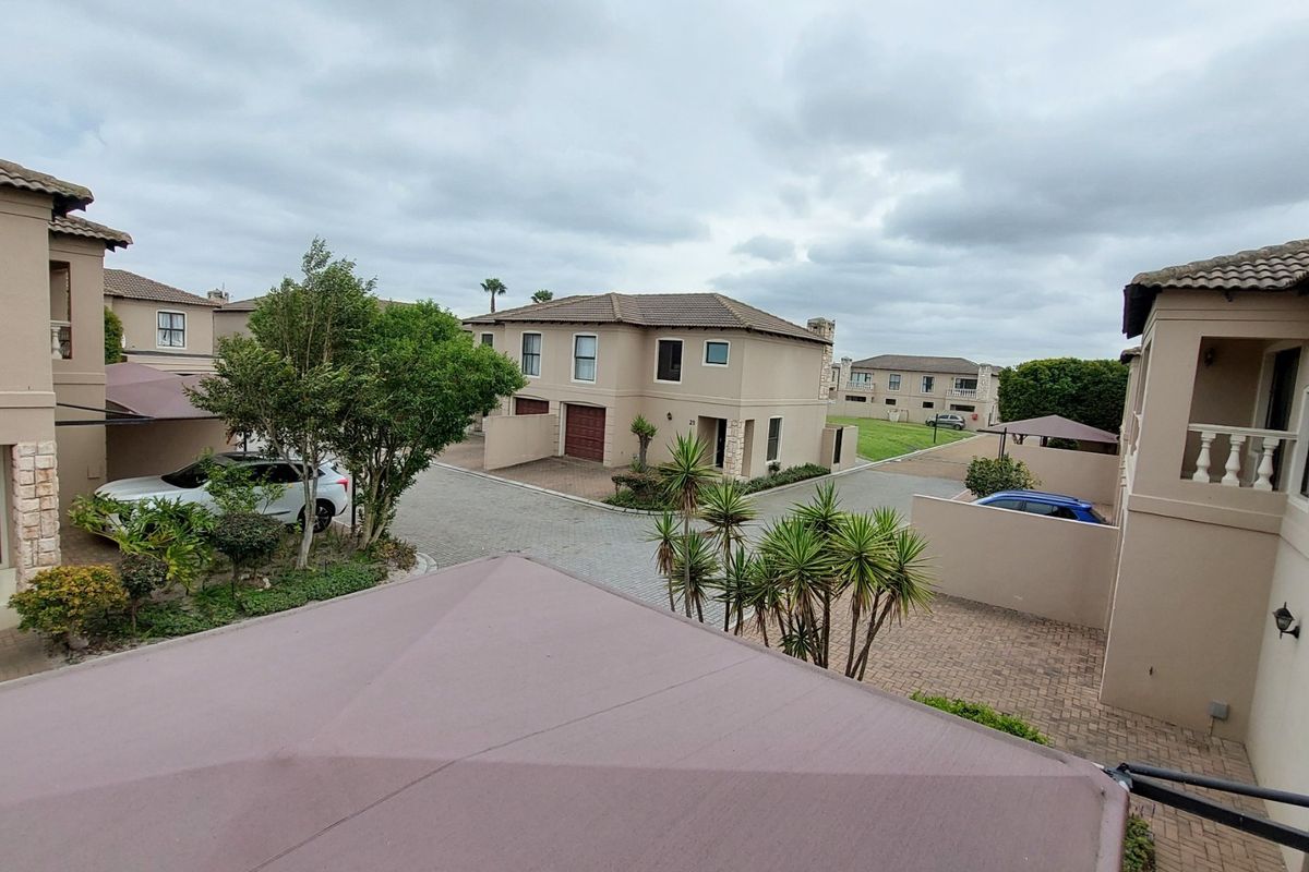 An elevated view of a townhouse complex courtyard featuring paved driveways, multiple residential units with tiled roofs, and established landscaping.