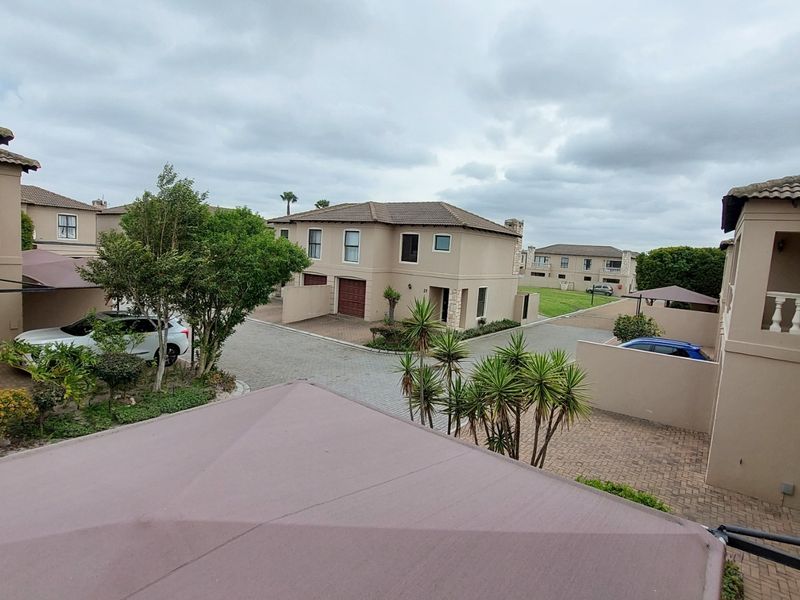 An elevated view of a townhouse complex courtyard featuring paved driveways, multiple residential units with tiled roofs, and established landscaping.