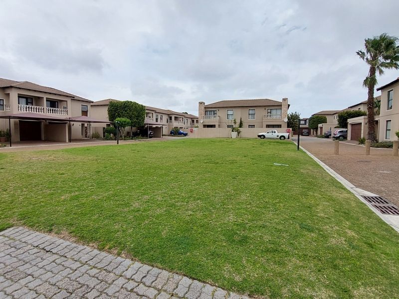 A wide-angle view of a townhouse complex featuring a central communal lawn, paved driveways, and multiple residential units with carports.