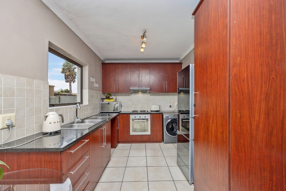 A functional kitchen featuring dark wood cabinetry, granite countertops, tiled flooring, and integrated appliances including an oven, hob, and extractor fan.