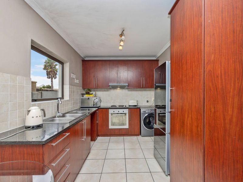 A functional kitchen featuring dark wood cabinetry, granite countertops, tiled flooring, and integrated appliances including an oven, hob, and extractor fan.