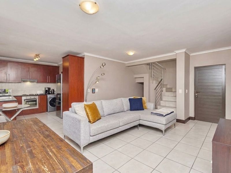 Open-plan living area featuring a modern kitchen with built-in cabinetry, tiled flooring, and a staircase leading to the upper level.