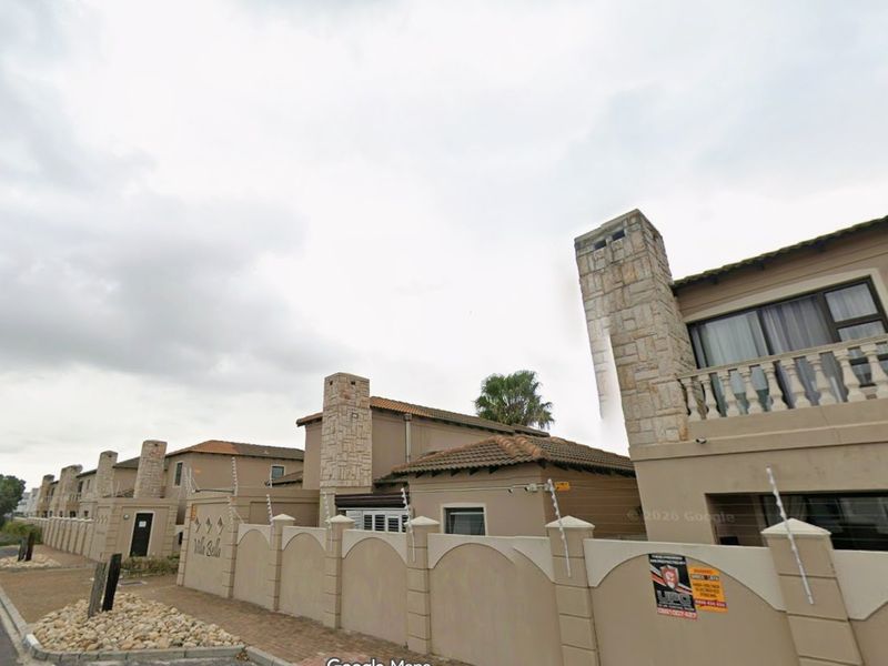 Street view of the townhouse complex featuring stone-clad chimneys, perimeter walls with electric fencing, and upper-level balconies.