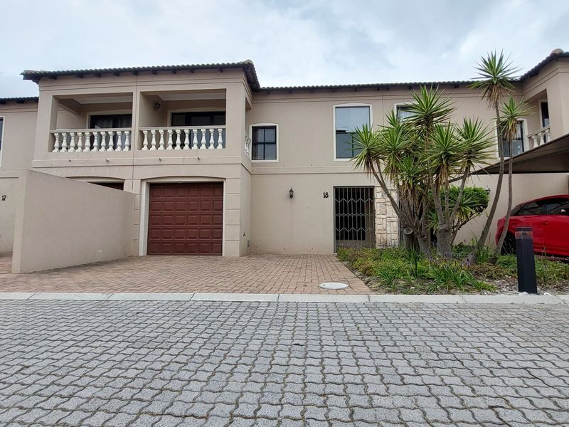 Front elevation of a two-story townhouse featuring a paved driveway, single garage, and an upper-level balcony with decorative balustrades.