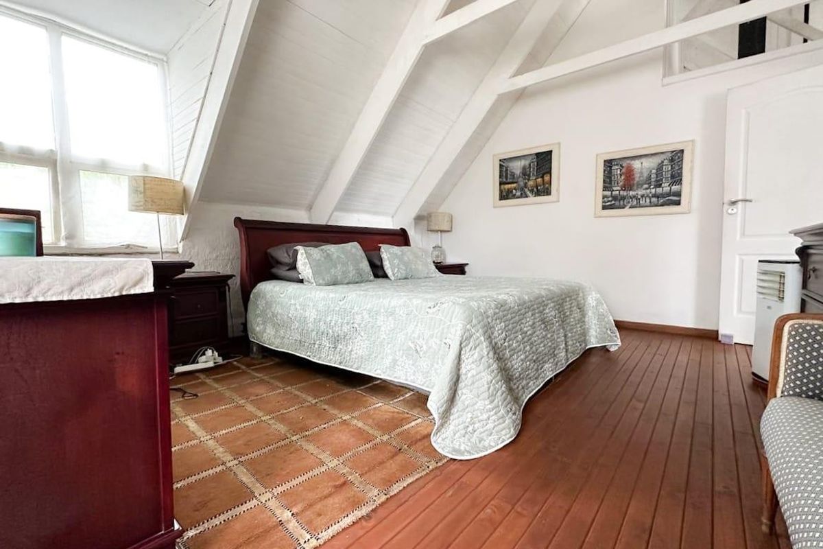 A charming attic-style bedroom featuring exposed timber rafters, warm wooden flooring, and natural light from the casement windows.