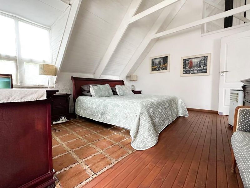 A charming attic-style bedroom featuring exposed timber rafters, warm wooden flooring, and natural light from the casement windows.