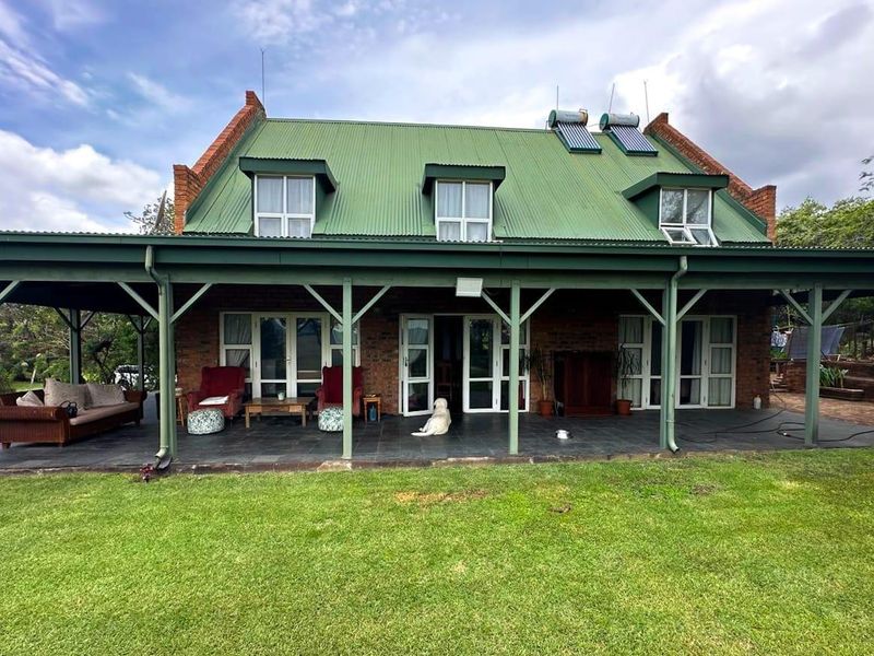 Rear view of a brick farmhouse featuring a green corrugated metal roof, solar water heating panels, dormer windows, and a spacious covered patio.