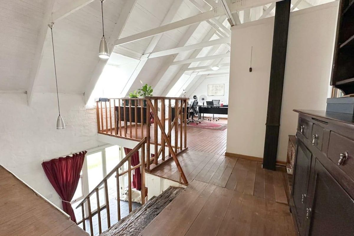 Spacious mezzanine living area featuring exposed timber roof trusses, wooden flooring, and natural light from skylights, overlooking the lower level.