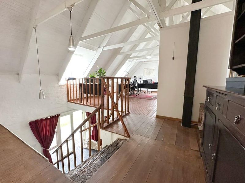 Spacious mezzanine living area featuring exposed timber roof trusses, wooden flooring, and natural light from skylights, overlooking the lower level.