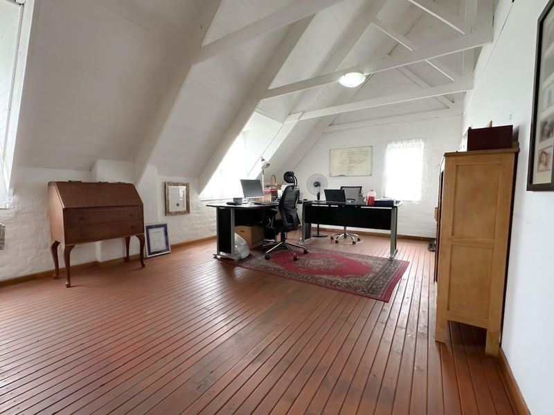 Spacious attic-style office featuring exposed timber roof trusses, warm timber plank flooring, and natural light from sloped skylight windows.