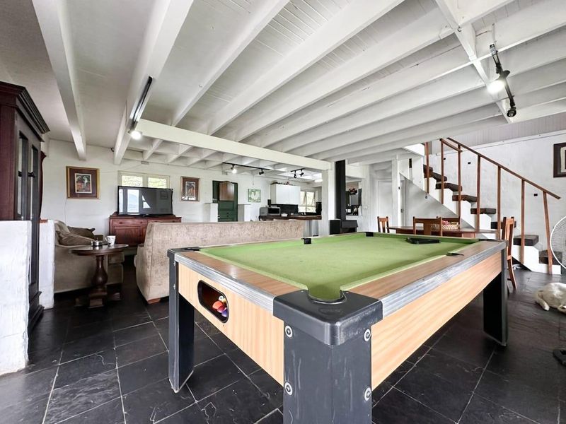 Spacious open-plan living area featuring exposed timber beam ceilings, slate tile flooring, a wood-burning fireplace, and a staircase leading to the upper level.