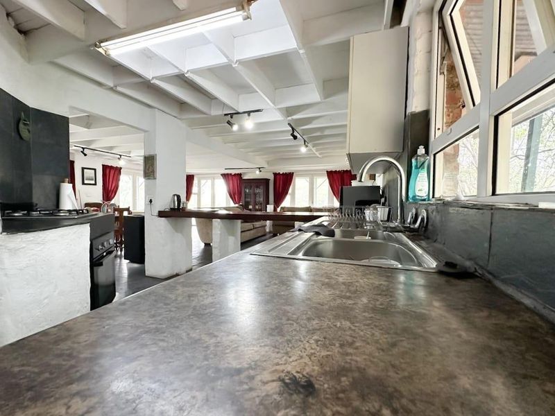 Open-plan kitchen and living area featuring exposed beam ceilings, a breakfast bar, and functional kitchen workspace with a double sink and built-in oven.