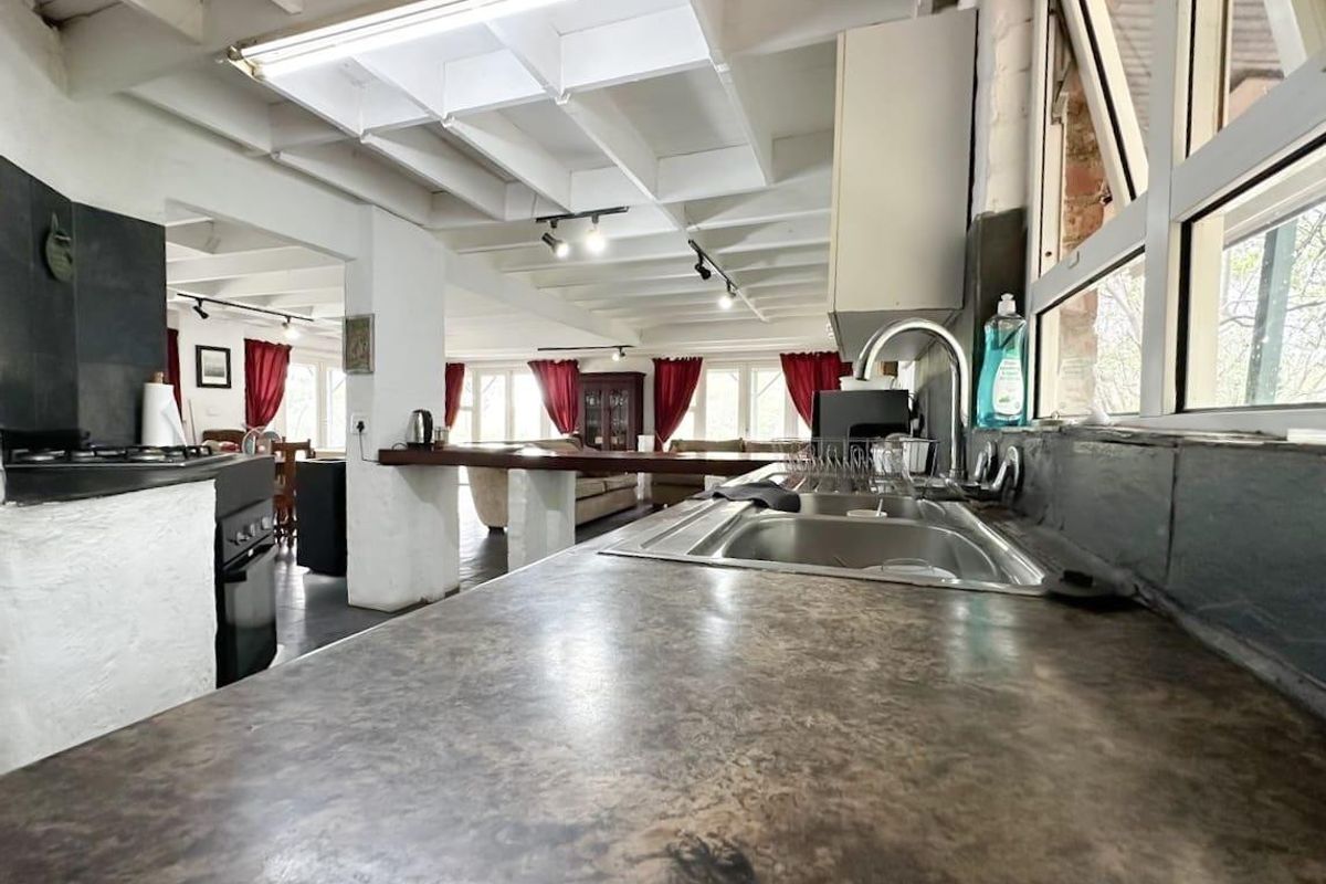 Open-plan kitchen and living area featuring exposed beam ceilings, a breakfast bar, and functional kitchen workspace with a double sink and built-in oven.