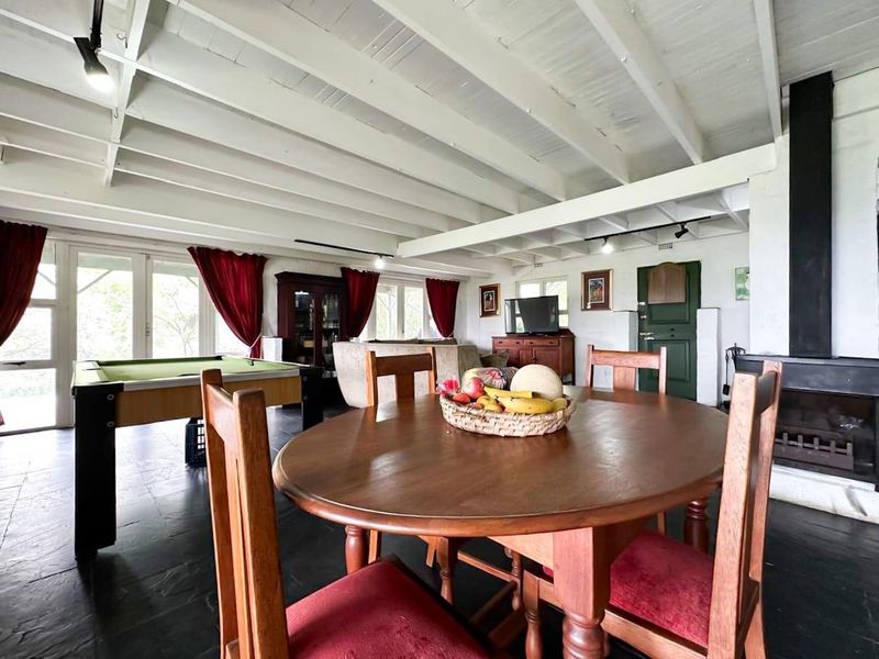 Spacious open-plan living and dining area featuring exposed beam ceilings, slate tile flooring, and a prominent freestanding fireplace.