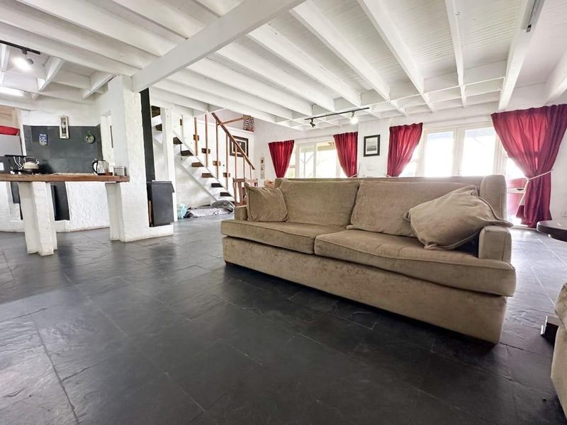 Spacious open-plan living area featuring exposed white timber beams, dark slate flooring, a central staircase, and a built-in fireplace.