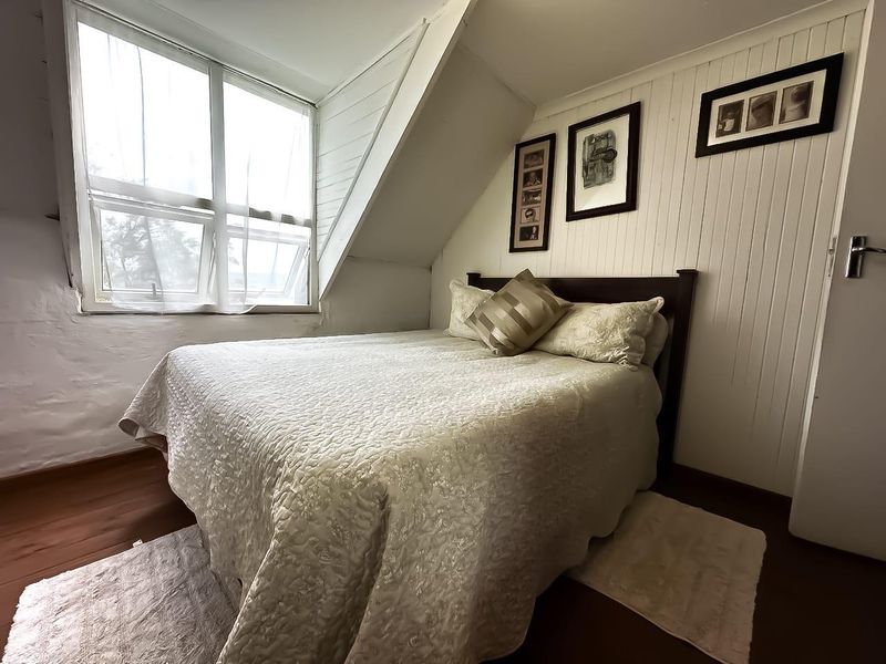 A cozy bedroom featuring sloped ceilings, timber wall paneling, and a large window providing natural light.