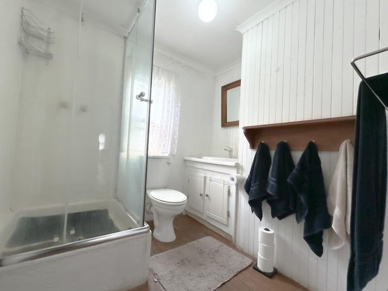 A functional bathroom featuring a glass shower enclosure, toilet, and vanity cabinet with classic tongue and groove wall paneling.
