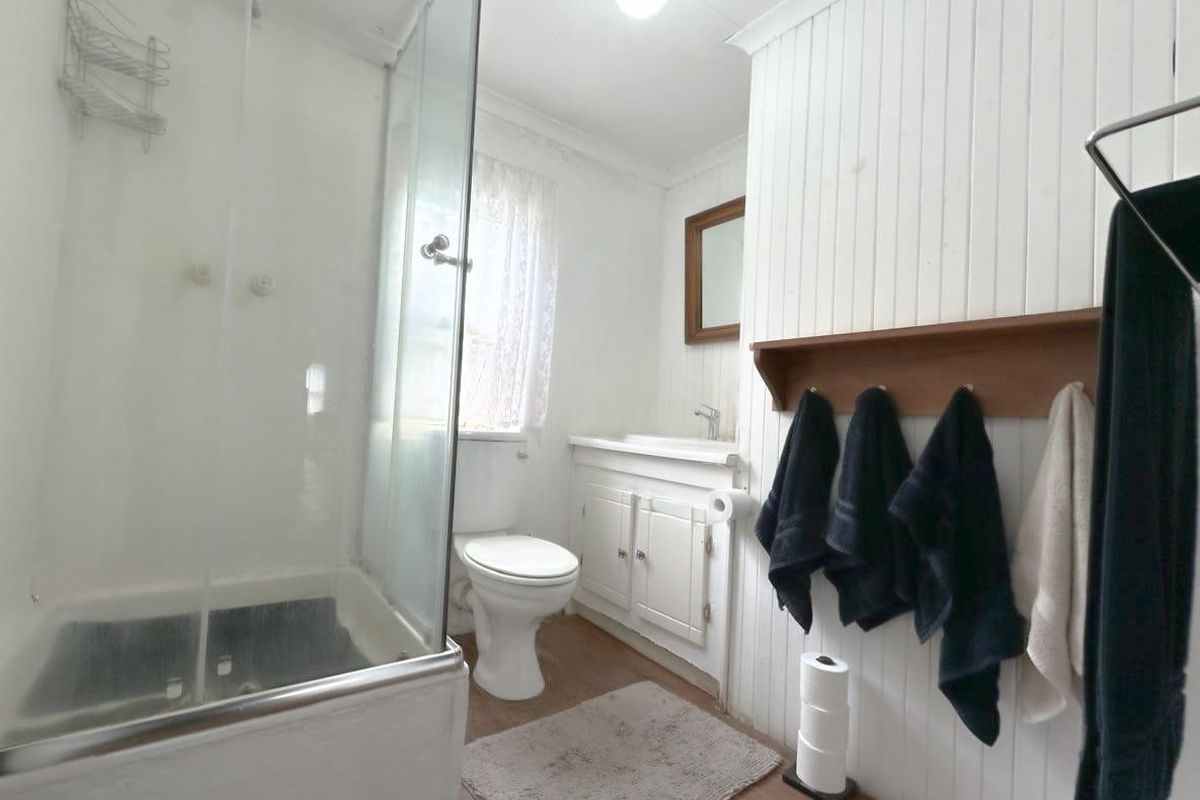 A functional bathroom featuring a glass shower enclosure, toilet, and vanity cabinet with classic tongue and groove wall paneling.