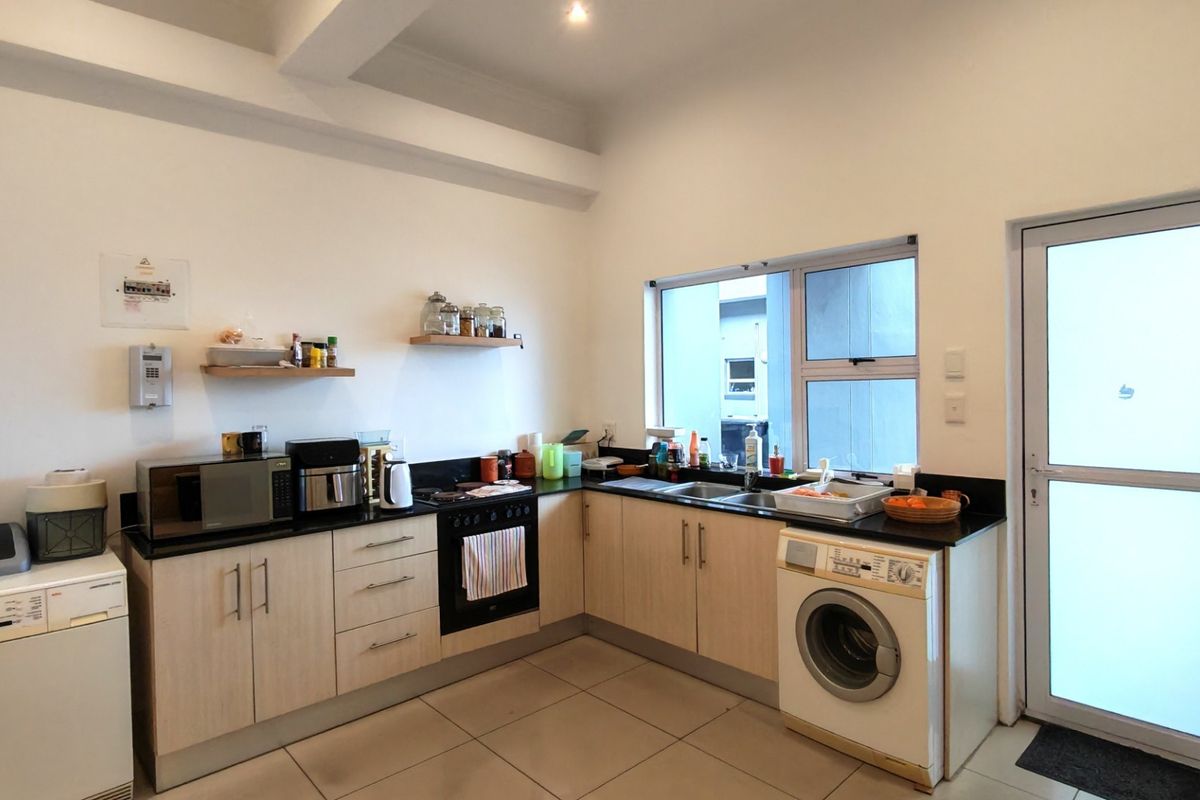 Functional kitchen featuring light wood-finish cabinetry, black granite countertops, integrated oven and hob, and direct access to an exterior door.