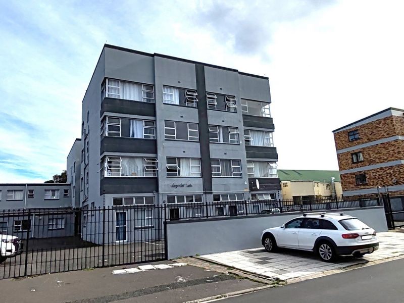 Front exterior view of a multi-story apartment building featuring a paved driveway and secure metal perimeter fencing.