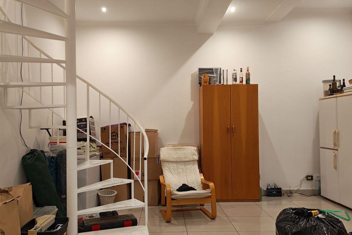 A living area featuring a white metal spiral staircase, recessed ceiling lighting, and neutral tiled flooring.