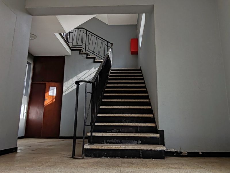 A communal apartment building hallway featuring a central staircase with metal handrails and tiled flooring.
