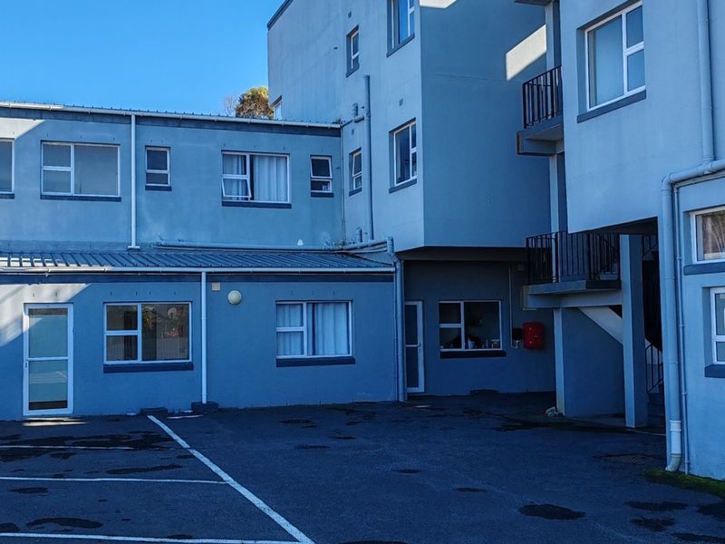 Rear exterior view of the apartment building featuring an asphalt parking area, metal roofing, and external access staircases.