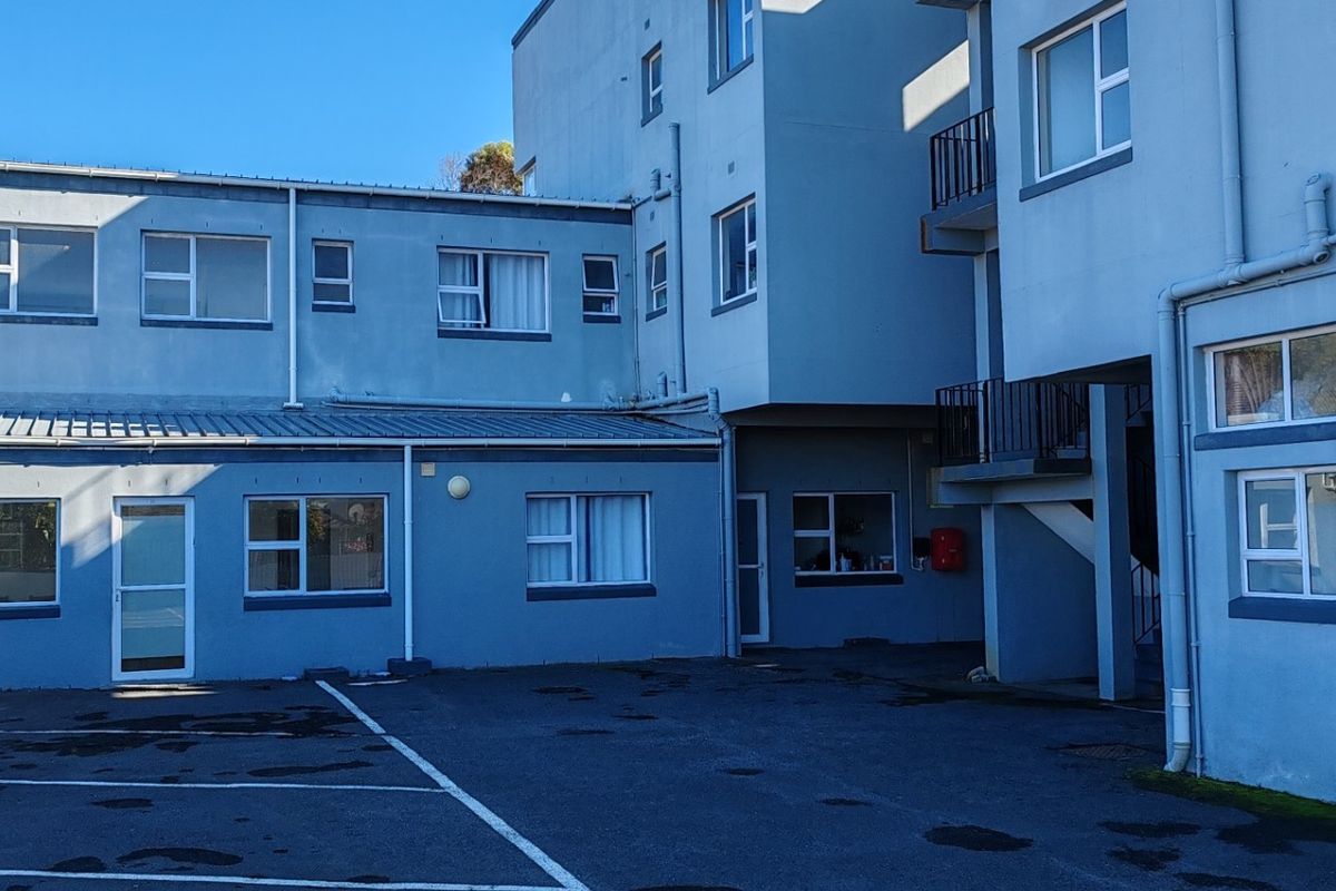 Rear exterior view of the apartment building featuring an asphalt parking area, metal roofing, and external access staircases.