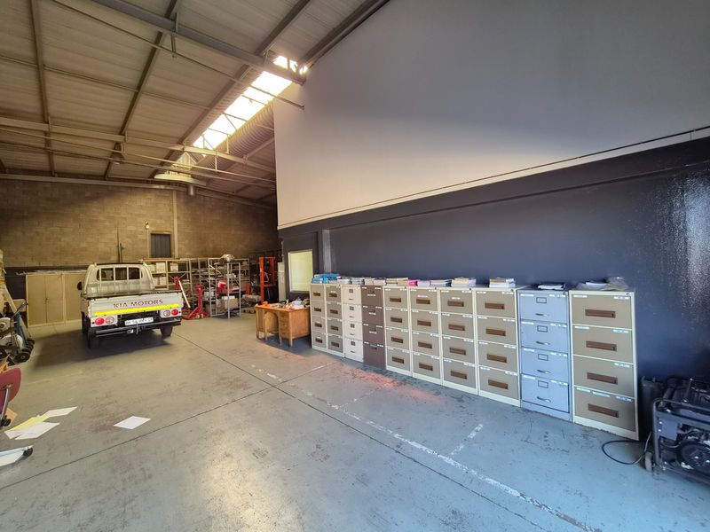 Spacious industrial utility area featuring high ceilings with exposed steel trusses, skylights, and durable concrete flooring, suitable for storage or workshop operations.
