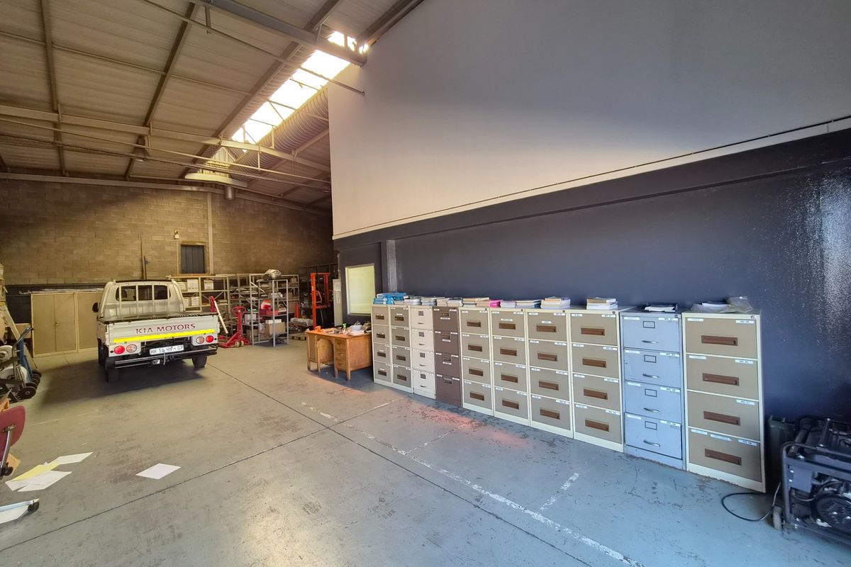 Spacious industrial utility area featuring high ceilings with exposed steel trusses, skylights, and durable concrete flooring, suitable for storage or workshop operations.