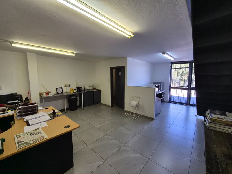 An industrial office space featuring tiled flooring, fluorescent lighting, a small kitchenette area, and a secure entrance gate.