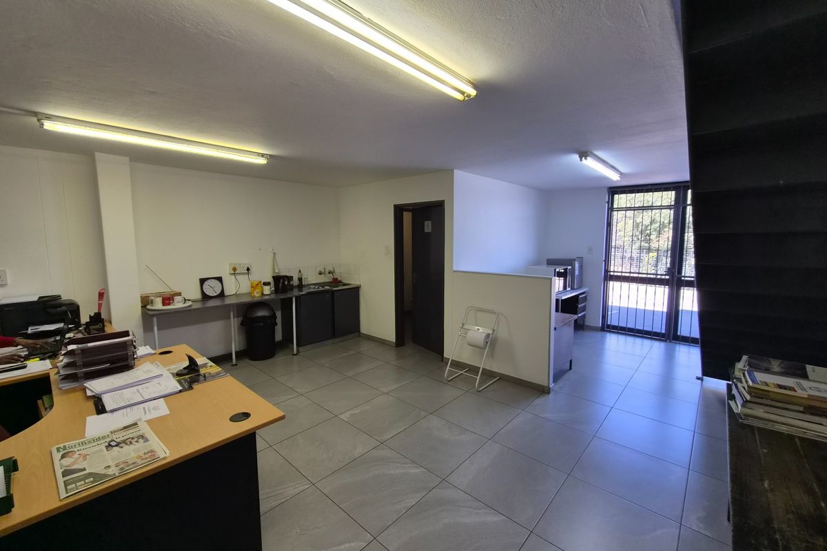 An industrial office space featuring tiled flooring, fluorescent lighting, a small kitchenette area, and a secure entrance gate.