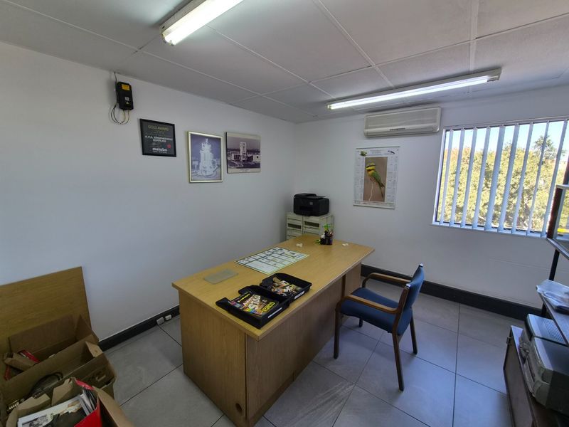 A functional industrial office space featuring tiled flooring, a drop ceiling, vertical blinds, and a wall-mounted split-system air conditioner.