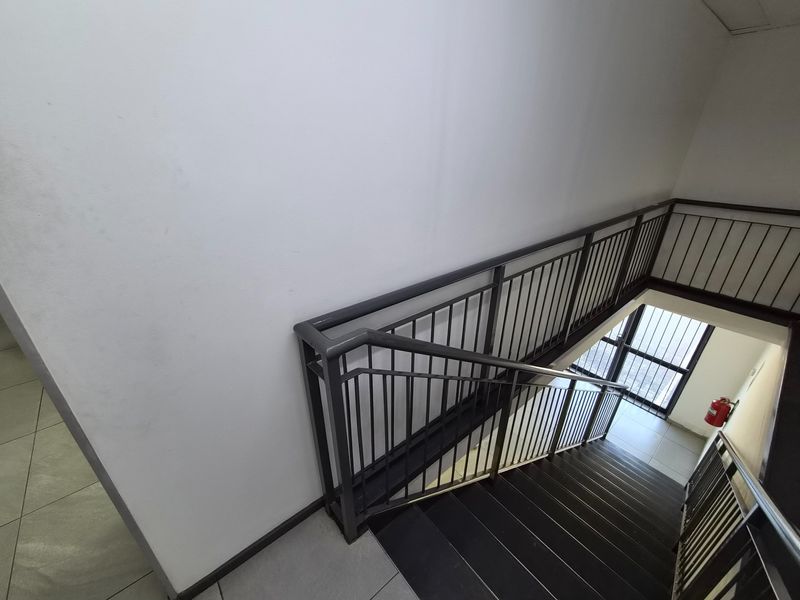 A clean, industrial-style stairwell featuring metal railings, tiled flooring, and a wall-mounted fire extinguisher.